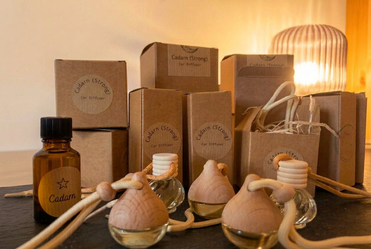 Cadarn (Strong) glass car diffusers with wooden caps, an amber refill bottle and branded kraft boxes, displayed beside a glowing lamp.