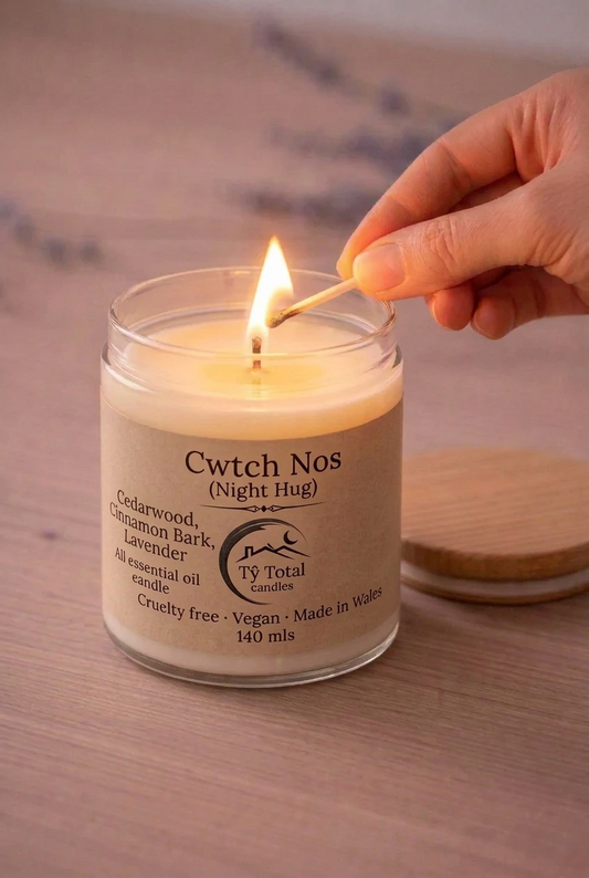 Cwtch Nos (Night Hug) cedarwood, cinnamon and lavender candle in a glass jar, being lit with a match.